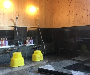 Tiled bath area with shower stations, yellow washing stools and wooden wall panels at Hoshi Meguri Shizuoka
