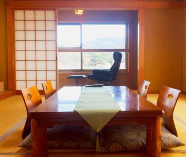 Sunlit tatami room with low wooden table, zabuton cushions, shoji screens and a window seat at Hoshi Meguri
