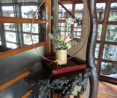 Ikebana vase on carved wooden stand beside circular mirror in Hoshidekan ryokan interior, Mie prefecture