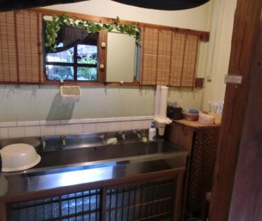 Compact wash area with stainless steel sink, wooden accents and a window with bamboo blinds at Hoshidekan Mie