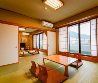 Traditional tatami room with low table, cushion chairs and large shoji windows overlooking mountains at Hoshikawakan, Nagano