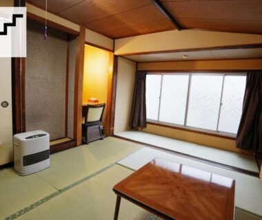 Traditional tatami room with low wooden table, curtained window and floor heater at Hostel Murasaki in Gifu