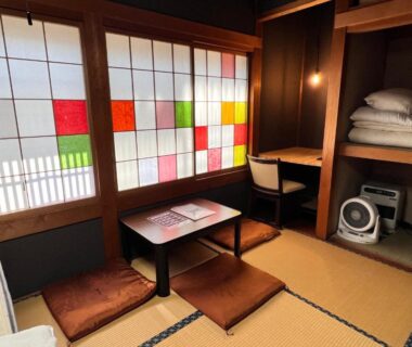 Tatami room with colorful shoji screens, low table, floor cushions and stacked futons at Hostel Murasaki in Gifu