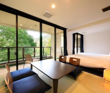 Tatami room with low table, cushions and twin beds opening to leafy balcony at Hot Spring Inn Hakone Suisen, Kanagawa