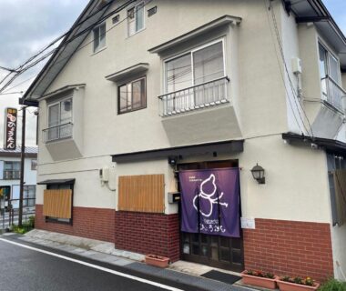 Two-story ryokan entrance with purple noren and brick lower facade on a street in Gunma, Kantō