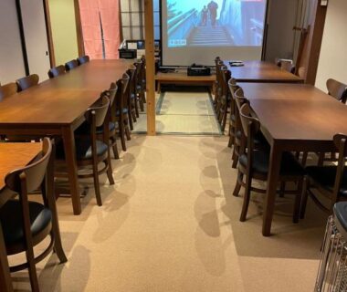 Long wooden tables and chairs facing a projector screen in a ryokan dining room at Hot Spring Inn Hyoutan, Gunma