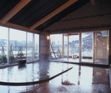Indoor onsen with wooden beams and large windows overlooking snowy hillside at a Niigata ryokan