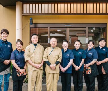 Smiling ryokan staff lined at the main entrance in uniforms outside Hot spring inn Snow country in Niigata, Chūbu