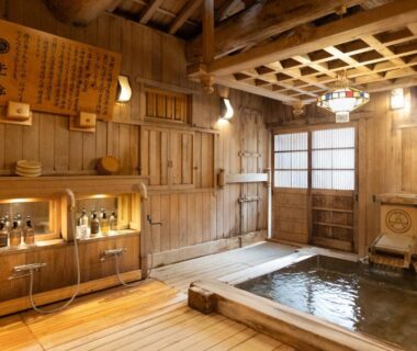 Traditional wooden indoor bath with soaking tub, shoji door, wooden floor and warm lantern lighting at Hotakajo, Nagano