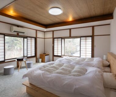 Spacious tatami room with low beds, shoji screens and large windows overlooking greenery at Hotakajo Ryokan in Nagano