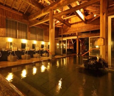 Wooden indoor onsen bath with washing stations and warm lighting at Hotel Futaba in Niigata, Chūbu, Japan