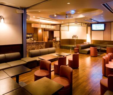 Warm lounge with sofas, low tables, round stools and wooden flooring at Hotel Futaba in Niigata, Chūbu