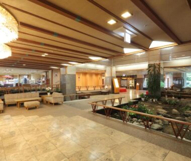 Tiled ryokan lobby with seating, wooden beams and indoor rock garden pond at Hotel Futaba Niigata