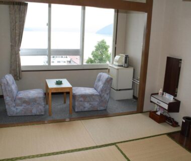 Tatami-floored guest room with low table, two chairs by window overlooking lake, small fridge and kettle