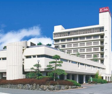 White multi-story ryokan building with landscaped entrance and surrounding hills in Yamanashi