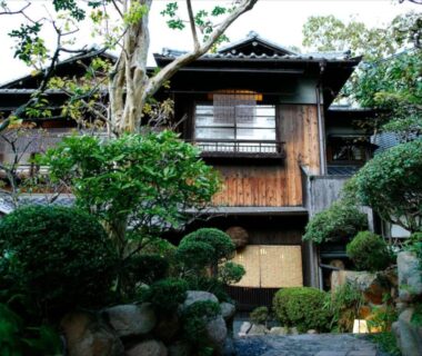 Two-story wooden ryokan facade with lattice windows, stone path and manicured garden at Hotel Hanakoyado in Hyōgo