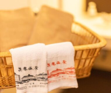 Embroidered towels folded in a woven basket on a bathroom counter at Hotel Hanamaki, Iwate Tōhoku