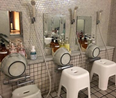 Communal wash stations with stools, handheld showers and toiletries at Hotel Harumoto, Tochigi, Kantō