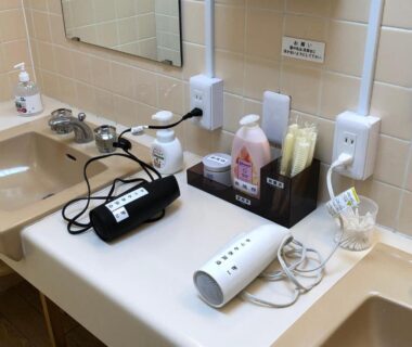 Bathroom sink and counter with hair dryer, toiletries and mirror at Hotel Harumoto in Tochigi, Kantō, Japan