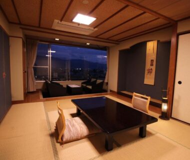 Tatami room with low table, cushions, sliding doors and window seating overlooking distant hills at Hotel Hatta in Yamanashi