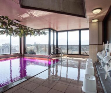 Indoor onsen with pink-lit tiled bath, washing stations and stools at Hotel Hatta, Yamanashi
