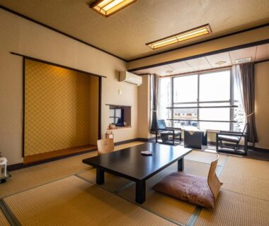 Bright tatami room with low table, floor cushions, decorative alcove and large window at Hotel Hatta, Yamanashi