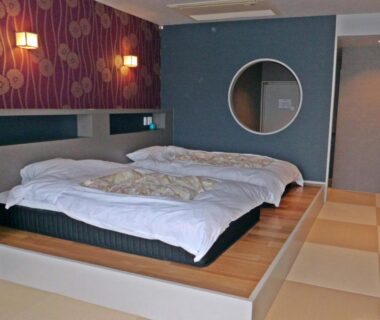 Raised platform beds on tatami-style flooring, circular mirror and bedside lamps at Hotel Heian in Yamanashi