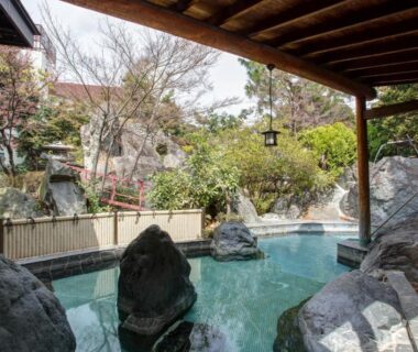 Rock lined outdoor onsen under wooden eaves at Hotel Heian in Yamanashi garden setting