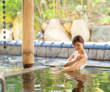 Woman relaxing in outdoor onsen with wooden pillars and stone garden at Hotel Hoho, Niigata