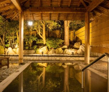 Covered outdoor onsen bath with wooden pavilion and stone edging, illuminated evening garden at Hotel Hoho, Niigata