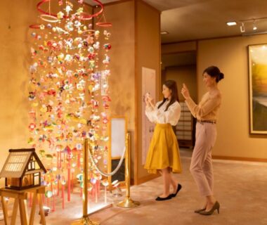 Warm ryokan lobby with hanging ornament display and two guests at Hotel Hoho, Niigata, Chūbu Japan