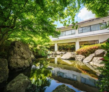 Reflective garden pond with rocks and maple trees beside Hotel Hoho building in Niigata