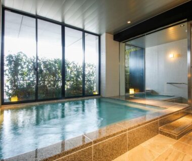 Modern indoor onsen with stone tiles and floor-to-ceiling windows at Hotel Honnoji, Kyoto