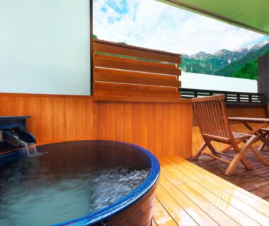 Round soaking tub on wooden deck with chairs and mountain view at Hotel Hotaka, Gifu