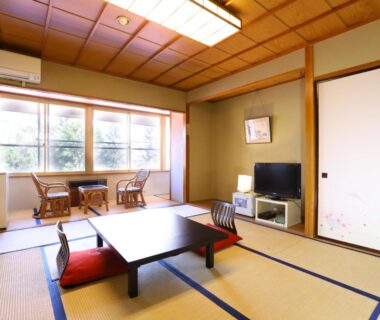 Traditional tatami room with low table, floor cushions, sliding fusuma doors and window seating with outside greenery