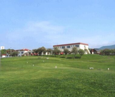 Expansive grassy foreground leading to Hotel Izumi building under blue sky in Hokkaidō