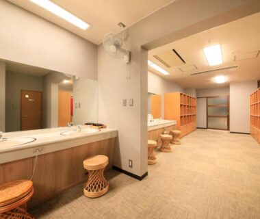 Communal changing area with sinks, mirrors, wooden stools and lockers at Hotel Kamogawaso in Hiroshima, Chūgoku