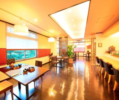 Warm-lit dining room with tables and counter seating overlooking greenery at Hotel Kamogawaso in Hiroshima