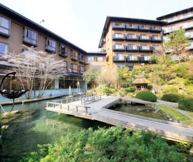Pond with wooden bridge and landscaped garden framed by Hotel Kamogawaso buildings in Hiroshima, Japan
