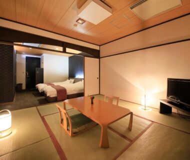 Traditional tatami room with low table, floor cushions and adjoining western bed area at Hotel Kamogawaso in Hiroshima