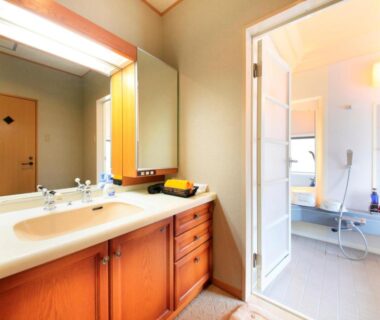 Wooden vanity with sink and mirror leading to tiled shower room at Hotel Kamogawaso, Hiroshima