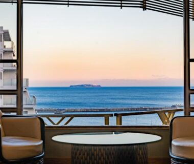 Seating area with round table and chairs facing the sea through a large window at Hotel Kan-ichi