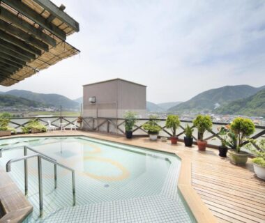 Outdoor onsen bath on rooftop deck at Hotel Kasuien overlooking harbor and green hills in Saga, Kyūshū