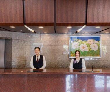 Two uniformed staff behind a polished reception counter with framed floral artwork in Hotel Kasuien lobby, Saga