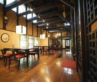 Interior view of a wooden dining hall with exposed beams, tables and lantern lighting at Hotel Kazahaya in Ōita