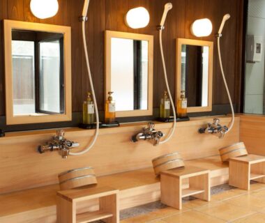 Row of wooden stools, handheld showers and mirrors in a ryokan bathing area at Hotel Kikori, Gifu, Chūbu