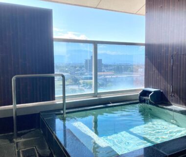 Balcony onsen bath with glass railing overlooking city and distant mountains at Hotel Kimiyoshi, Yamanashi