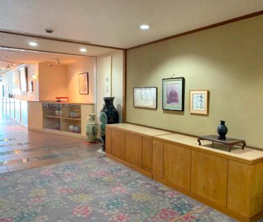 Carpeted ryokan corridor with wooden display cabinet, decorative vases and framed artwork at Hotel Kimiyoshi in Yamanashi