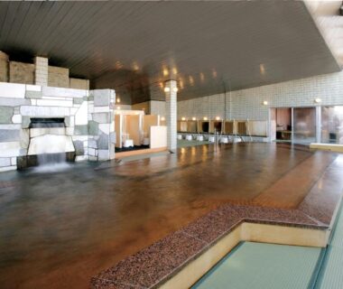 Large communal indoor bathing hall with tiled feature wall and steps at Hotel Kimura in Gunma, Kantō