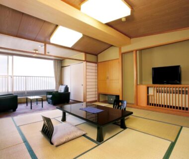 Spacious tatami room with low table, zabuton cushions, TV and window seating at Hotel Kimura in Gunma, Japan